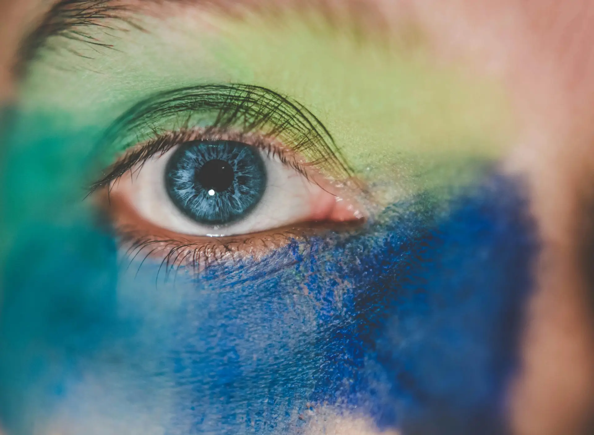 Detailed close-up of a human eye with vibrant artistic makeup, emphasizing colors and striking detail.