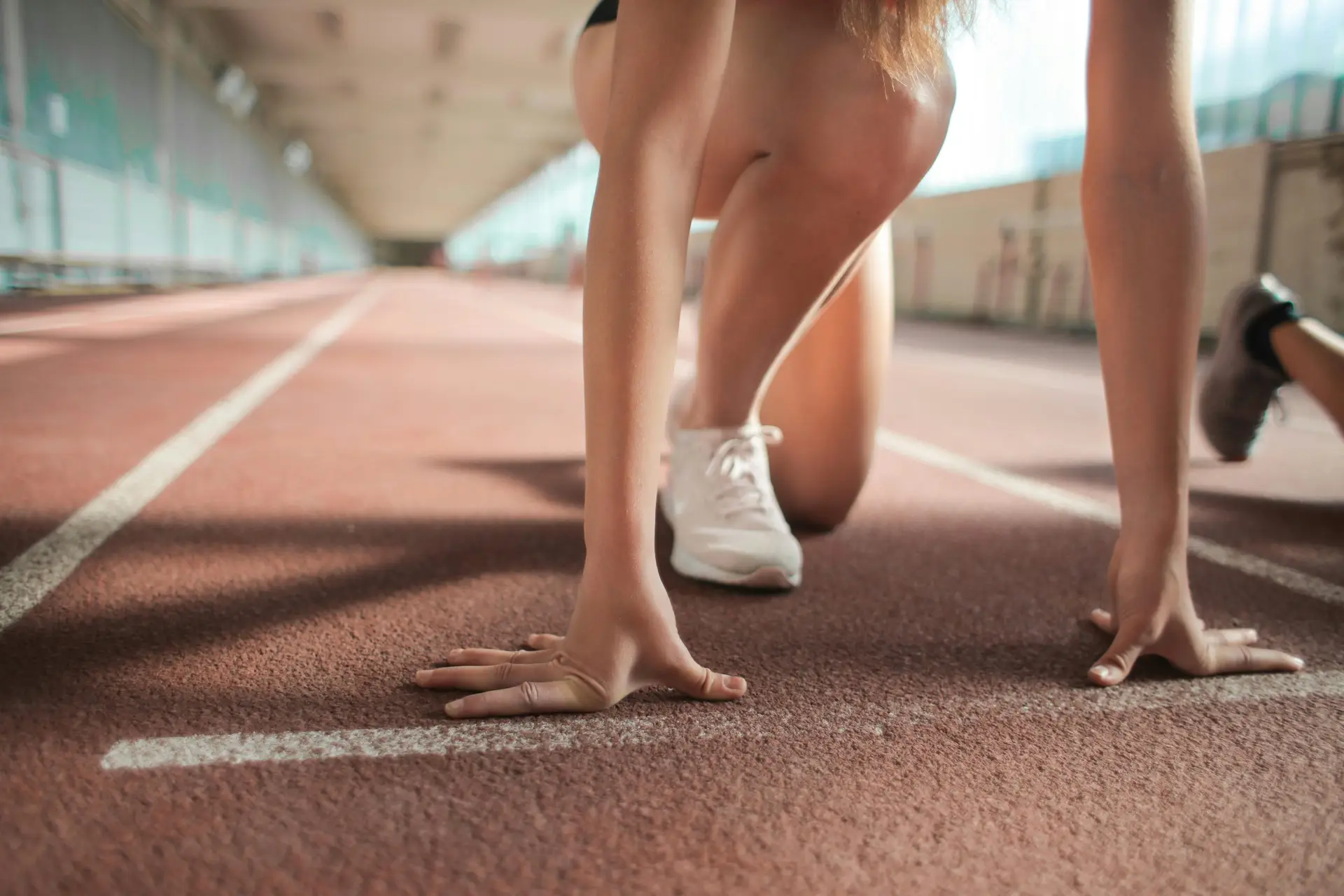 Focused female athlete in crouch start position preparing to sprint on an indoor track.